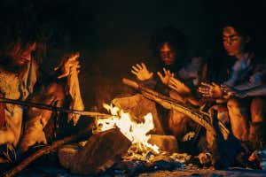 Neanderthal or Homo Sapiens Family Cooking Animal Meat over Bonfire and then Eating it. Tribe of Prehistoric Hunter-Gatherers Wearing Animal Skins Eating in a Dark Scary Cave at Night; Shutterstock ID 1595983549; purchase_order: -; job: -; client: -; other: -