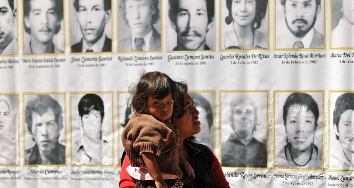 A woman with her daughter observes the pictures of people who lost their lives during the Guatemalan civil war, as forensic anthropologists from the Forensic Anthropology Foundation of Guatemala (FAFG) exhume the bodies of one of four mass graves in La Verbena cemetery, in Guatemla City on March 6, 2010, as part of a search to find the 889 people who disappeared during the internal armed conflict (1960-1996). AFP PHOTO/Johan ORDONEZ (Photo credit should read JOHAN ORDONEZ/AFP via Getty Images)
