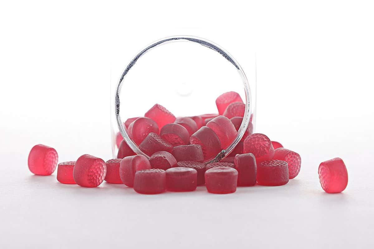 Red melatonin gummies spill out of a clear container in front with a white background