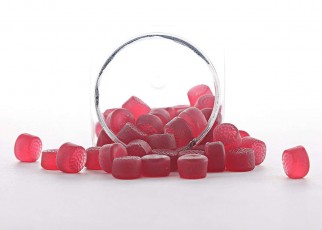 Red melatonin gummies spill out of a clear container in front with a white background