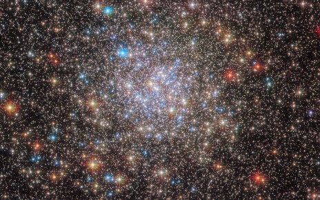 A dense collection of stars covers the view. Towards the centre the stars become even more dense in a circular region, and also more blue. Around the edges there are some redder foreground stars, and many small stars in the background.