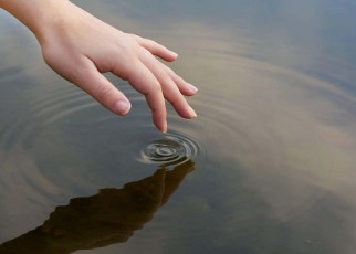 2J1JM3H Patterns in a pond. Cropped shot of a finger touching water to form ripples.