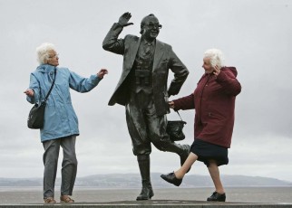 MORCAMBE, UNITED KINGDOM - JUNE 22: Despite inclement weather pensioners raise a happy smile as they perform the famously British dance of comedians Morcambe and Wise next to a statue of Eric Morcambe, at Morcambe Bayon June 22, 2006, in Morcambe, England. Confidence & Happiness specialist, Scientist Cliff Arnall from the University of Cardiff has identified June 23, 2006 as being the happiest day of the year. His calculations were based on outdoor activity, nature, social interaction, childhood summers, positive memories, temperature and holidays. (Photo by Christopher Furlong/Getty Images)