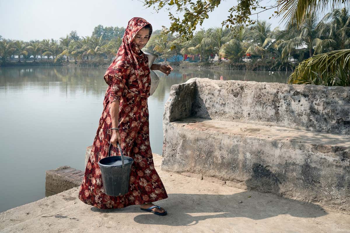 A woman collects water from a pond excavated by the government with the help of a nonprofit organisation in the 'Dristinaondon' area.