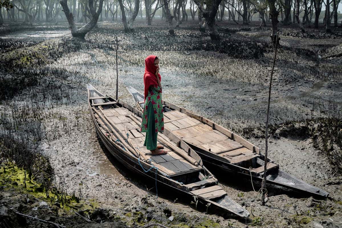 Aklima Parvin (19) keeps har face covered as she stands in a boat stranded on a mud flat. She faces discrimination due to her skin discolouration and pigmentation. She stopped going to college and spends her days alone since many of her friends are now married and have left the area.