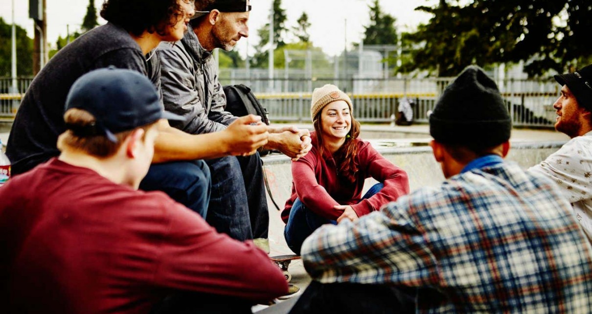 Group of young skateboarders sitting in discussion with mature skateboarder in neighborhood skate park