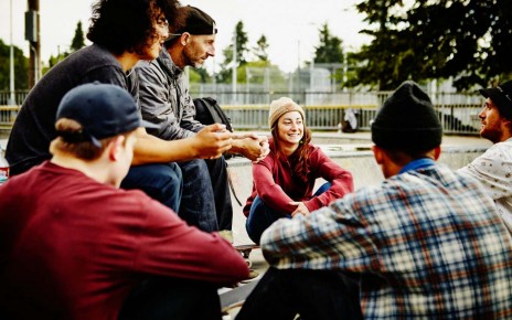 Group of young skateboarders sitting in discussion with mature skateboarder in neighborhood skate park