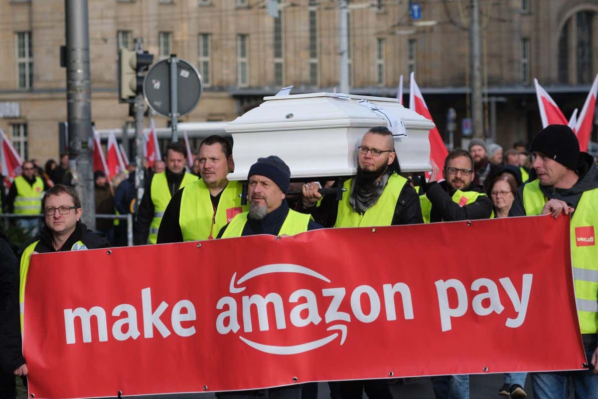 2KJXNKB Leipzig, Germany. 25th Nov, 2022. Participants of a demonstration of the trade union Verdi walk with flags and carry a banner with the inscription "Make Amazon pay" and a coffin. About 200 employees of the online mail order company Amazon protested for better working conditions and adequate pay. Credit: Sebastian Willnow/dpa/Alamy Live News