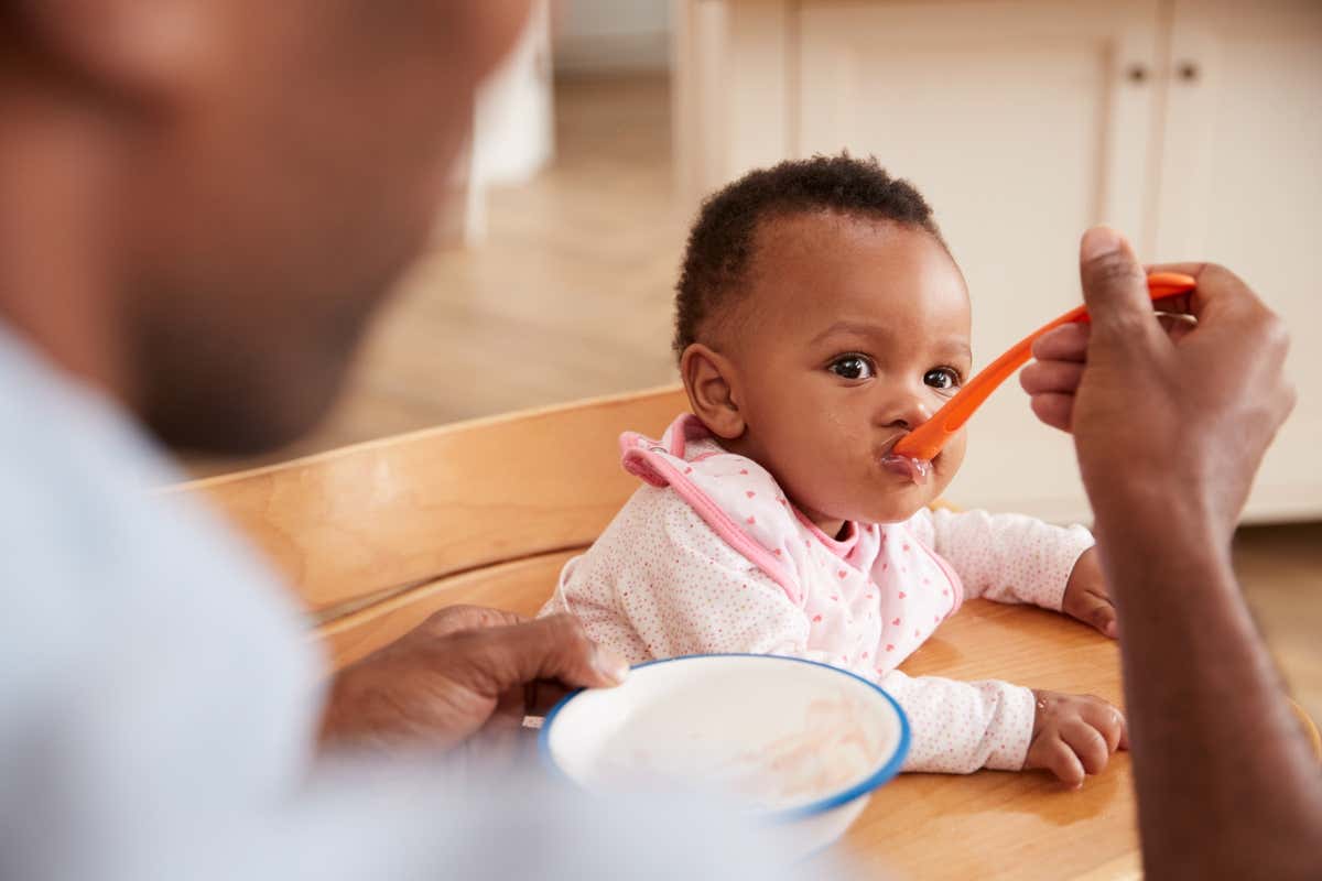 A person feeds their daughter using a spoon. Your diet at an early age can affect how your microbiome develops