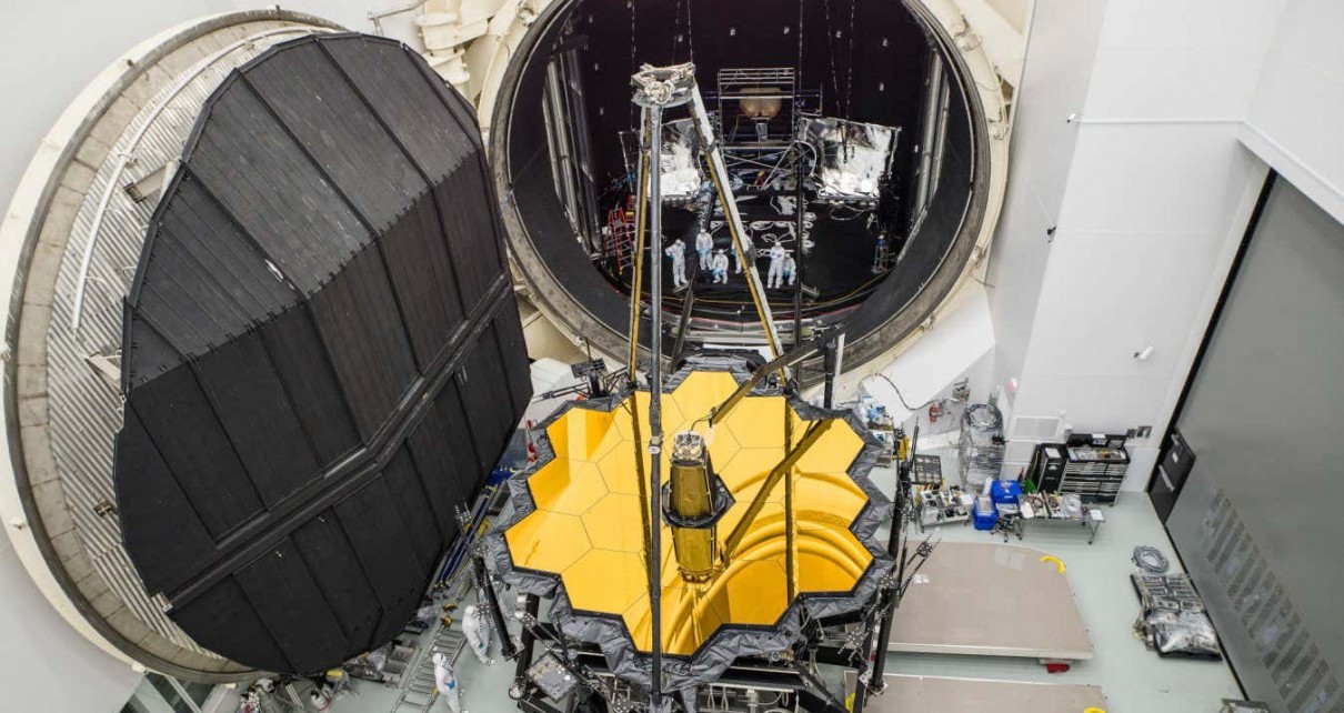 A fully deployed OTIS, with the secondary mirror extended over the primary mirror, is removed from Chamber A after a successful thermal-vacuum test in 2017. Seen still in the chamber is a sunshield simulator, called the L5 Simulator, representing the fifth and innermost layer of the sunshield. The telescope would be shipped to the Northrop Grumman facility in California to be integrated with the real sunshield. I was suspended on a lift for this shot. Page 119