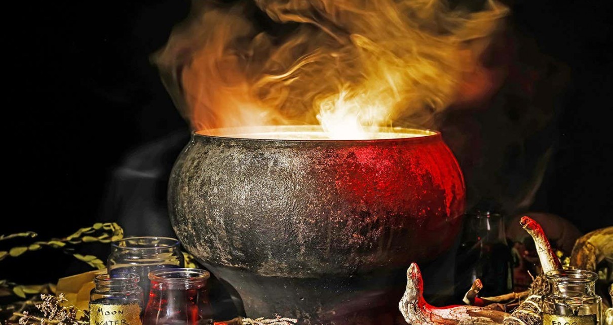 Witch's cauldron with potion and different magic attributes for ritual on dark background