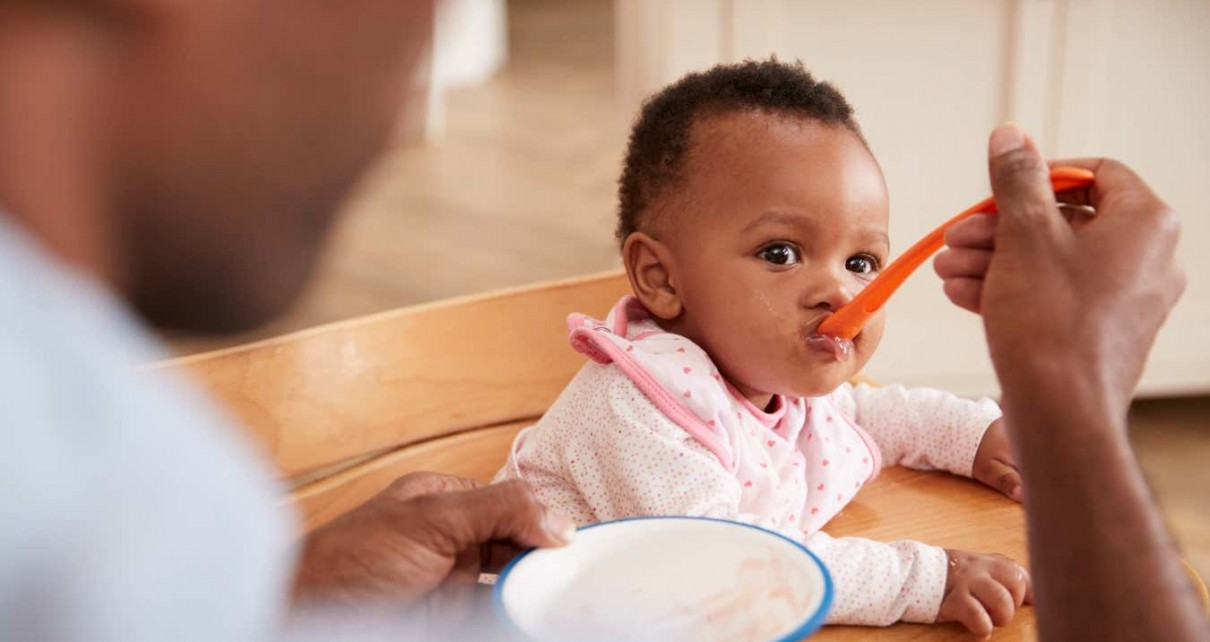 A person feeds their daughter using a spoon. Your diet at an early age can affect how your microbiome develops