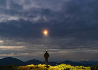 The UFO shines on a male standing on the mountain; Shutterstock ID 1476587882; purchase_order: -; job: -; client: -; other: -