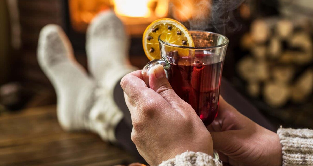 GTG9F9 Hot mulled wine and book in woman hands. Relaxing in front of burning fire in the cold winter day.