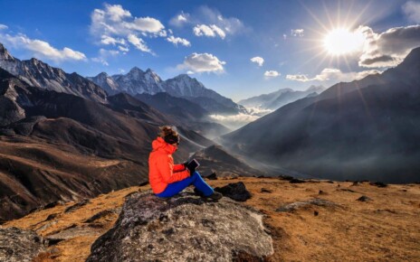 Young woman, wearing a orange jacket, is reading a book on an ebook reader during sunset over Himalayas. She is sitting on the top of a mountain and holding the e-reader.The afternoon sun on the background. Mount Everest National Park. This is the highest national park in the world, with the entire park located above 3,000 m ( 9,700 ft). This park includes three peaks higher than 8,000 m, including Mt Everest. Therefore, most of the park area is very rugged and steep, with its terrain cut by deep rivers and glaciers. Unlike other parks in the plain areas, this park can be divided into four climate zones because of the rising altitude. The climatic zones include a forested lower zone, a zone of alpine scrub, the upper alpine zone which includes upper limit of vegetation growth, and the Arctic zone where no plants can grow.