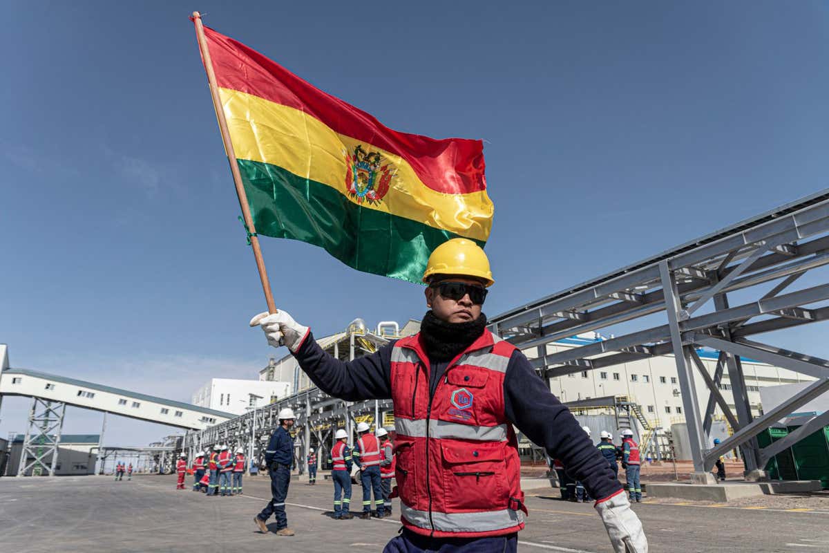 A worker holds the Bolivian flag during the inauguration of the new state-owned Yacimientos de Litio Bolivianos (YLB) lithium carbonate production facility, inside the Uyuni Salt Flats near Uyuni, Potosi Department, Bolivia, on Friday, Dec. 15, 2023. Bolivia is cutting the ribbon on its first industrial-scale lithium plant, the dawn of what it hopes will be an export boom of the battery metal that could bring it back from the brink of economic crisis. Photographer: Marcelo Perez del Carpio/Bloomberg via Getty Images