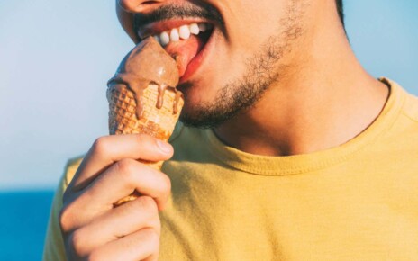 2C6AJB8 young man in yellow licks his chocolate ice cream