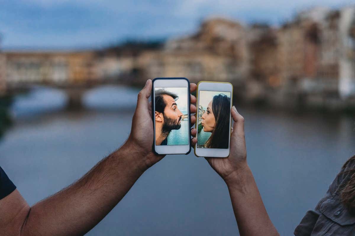 Conceptual shot of a young adult couple kissing via mobile phone