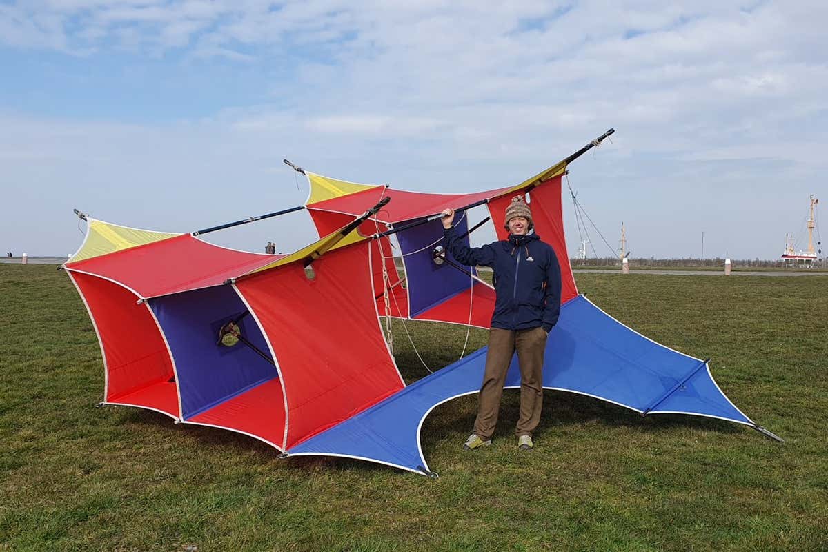 A man standing next to a large red-and-blue kite that will study the total solar eclipse