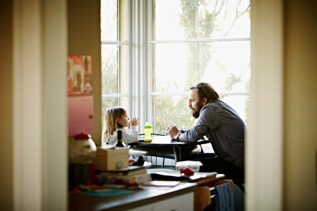 Father and daughter sitting at kitchen table near window in discussion