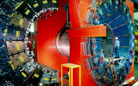 CDF particle detector at the Fermi National Accelerator Laboratory (Fermilab) near Chicago, USA. The CDF (Collider Detector Facility) records subatomic particles created in high-energy proton-antiproton collisions in the Tevatron coll- ider. It co-discovered the top quark in 1994. Here the detector is partly disassembled between operation runs. The black segments (left) are part of the outer muon chambers. The red areas are part of the magnet which bends charged particles travelling out from the collision point. The blue segments (right) are part of the hadron calorimeter. When in use these parts are closed tightly together. Photographed in 1998. The physicist is ROB ROSER.