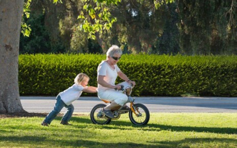 E3Y70G Three year old boy pushing grandmother on cycle in park